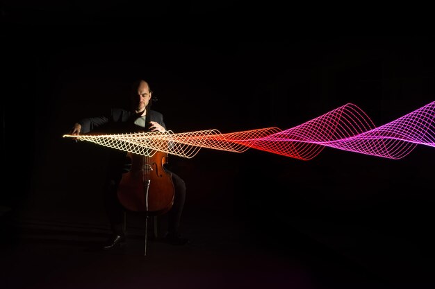 Lunghezza completa di un musicista che suona il violoncello con una pittura luminosa su uno sfondo nero