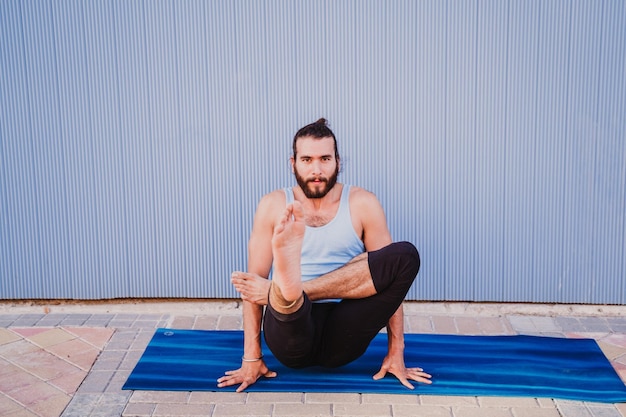 Lunghezza completa di un uomo che esegue yoga su un tappetino da esercizio contro la parete