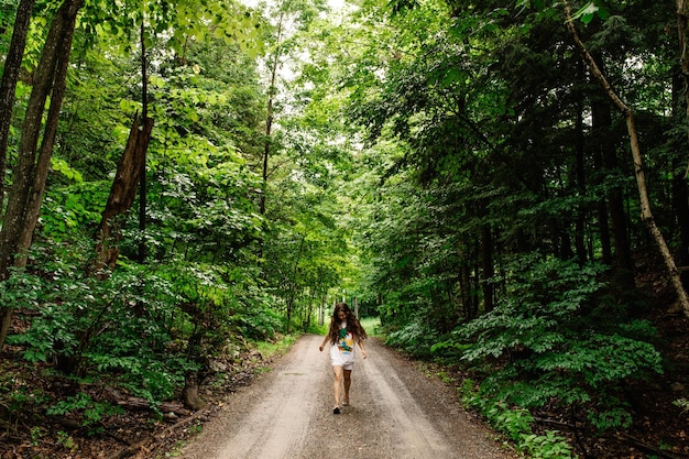 Lunghezza completa di una donna che cammina su una strada di terra nella foresta