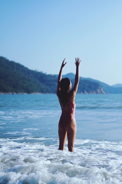 Lunghezza completa di una donna con le braccia alzate in piedi sulla spiaggia