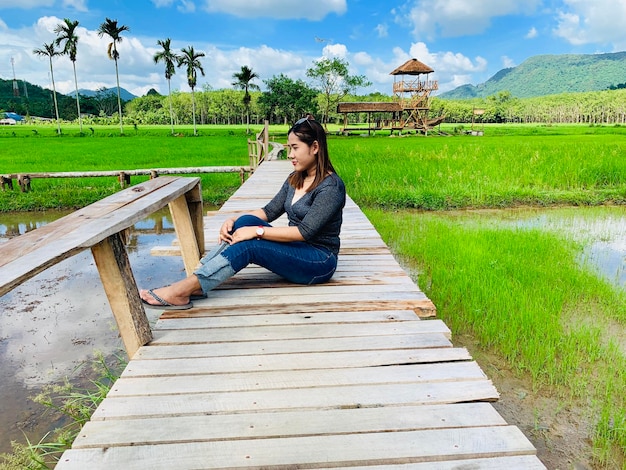 Lunghezza completa di una donna seduta su un ponte pedonale sopra un campo di riso