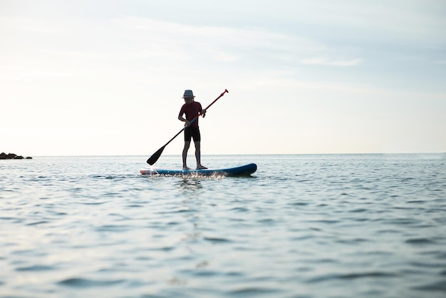 Lunghezza completa di una ragazza che fa paddleboard sul mare contro il cielo