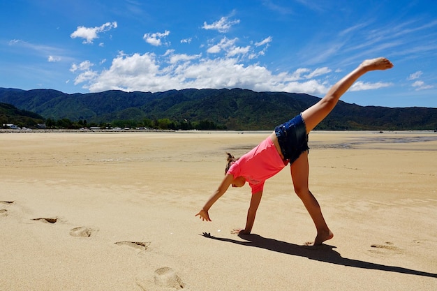 Lunghezza completa di una ragazza che fa una ruota su una spiaggia deserta contro il cielo