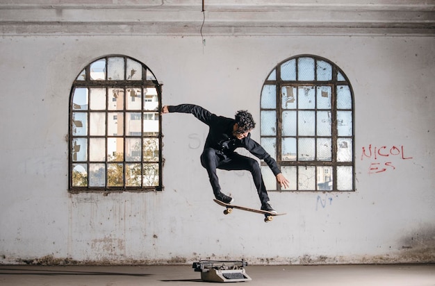 Lunghezza completa di uomo che fa skateboard contro le finestre