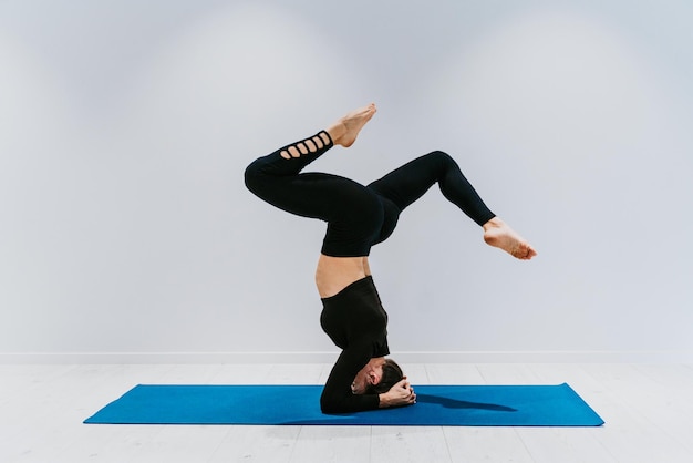 Lunghezza intera di una donna che esegue il headstand su uno sfondo bianco