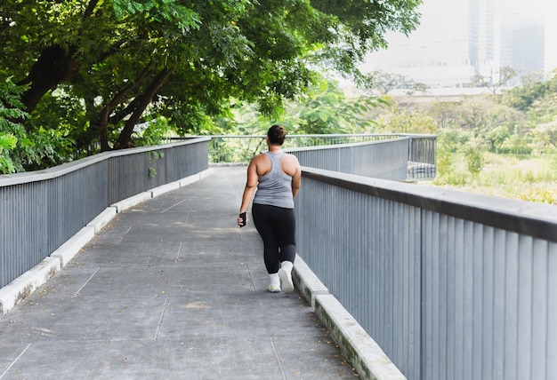 Lunghezza piena di donna asiatica in sovrappeso che cammina all'aperto sul ponte nel parco della città