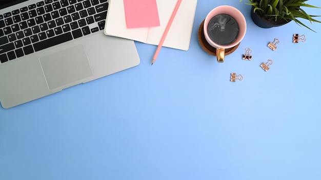 Luogo di lavoro creativo con la tazza di caffè del taccuino del computer portatile e lo spazio della copia su fondo blu