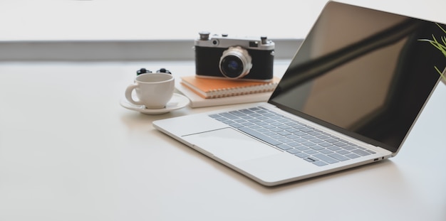 Luogo di lavoro minimal fotografo con laptop aperto, macchina fotografica d'epoca e una tazza di caffè