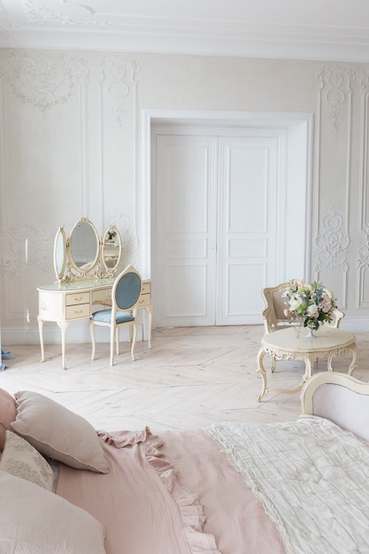 Lussuosi interni luminosi in stile barocco. Una camera spaziosa con bei mobili chic da strada, un camino e fiori. stucco vegetale alle pareti e parquet in legno chiaro