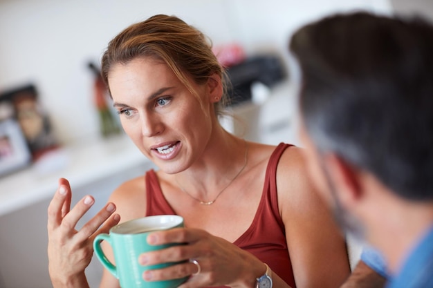 Ma questo è esattamente quello che sto dicendo Foto ritagliata di una giovane donna attraente che ha una conversazione seria con suo marito mentre tiene una tazza di caffè