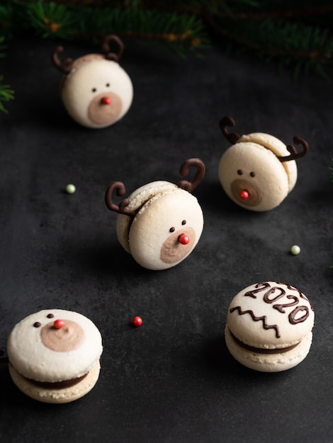 Macaron naso rosso renna e macaron con numero 2020 con abete brances su sfondo nero scuro. Carta di Natale e Capodanno
