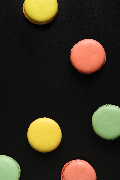 Macaroni francesi brillanti su uno sfondo nero vista dall'alto Assortimento di macaroni multicolori con diversi sapori Deliziosi pasticcini a piatto sfondo alimentare Dolci