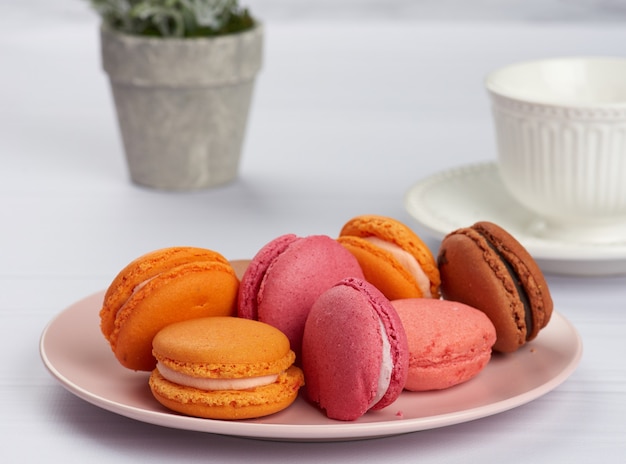 Macarons al forno su un piatto rosa, dietro una tazza bianca in ceramica con caffè, mattina