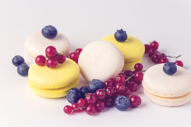 Macarons colorati francesi Macarons bianchi e gialli su sfondo blu con ribes rosso fresco