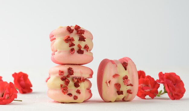 Macarons e boccioli di rosa alla fragola rossa al forno su un tavolo bianco, dessert gourmet di farina di mandorle, primo piano