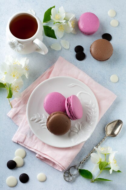 Macarons francesi al cioccolato e ribes nero in piatto di ceramica su cemento leggero.