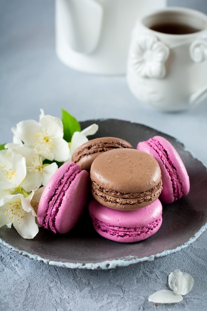 Macarons francesi al cioccolato e ribes nero in piatto di ceramica su cemento leggero.