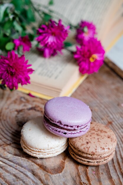 Macarons sfondo fiori rossi e libri, su un tavolo di legno. Cornice verticale. Estetica con amaretti e fiori. Bellissime torte su un tavolo di legno. Mattina colazione francese.