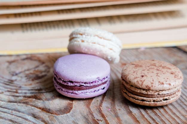 Macarons sullo sfondo del libro, su un tavolo di legno. telaio orizzontale. Estetica con amaretti e un libro. Bellissime torte su un tavolo di legno