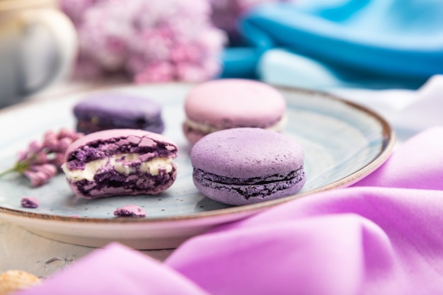 Macarons viola o torte di amaretti con una tazza di caffè su uno sfondo di cemento bianco e tessuto magentablue. Vista laterale, primo piano,