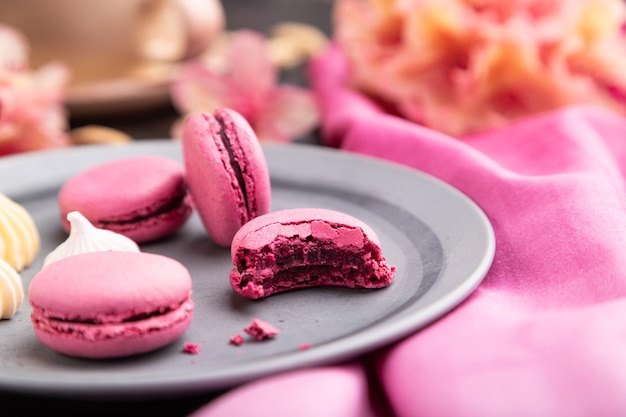 Macarons viola o torte di amaretti con una tazza di caffè su uno sfondo di cemento nero e tessuto rosa. Vista laterale, primo piano, messa a fuoco selettiva.