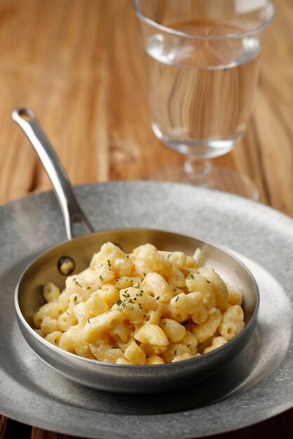 Maccheroni cremosi e formaggio su una padella con parmigiano ed erbe aromatiche, isolati su un tavolo di legno