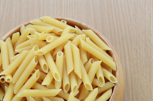 Maccheroni crudi nella ciotola di legno su fondo di legno.