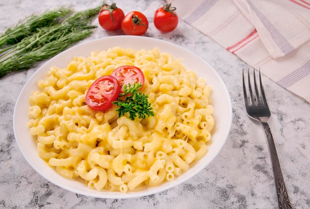 Maccheroni e formaggio su un piatto bianco con prezzemolo e pomodorini su sfondo grigio Mac e formaggio americano