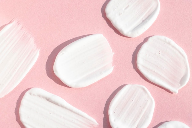 Macchie di corpo bianco e crema per il viso su fondo rosa piatto Campione di prodotto cosmetico