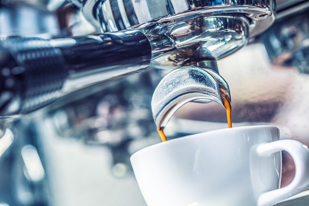 Macchina da caffè del primo piano che versa il caffè espresso caldo dentro alla tazza bianca.