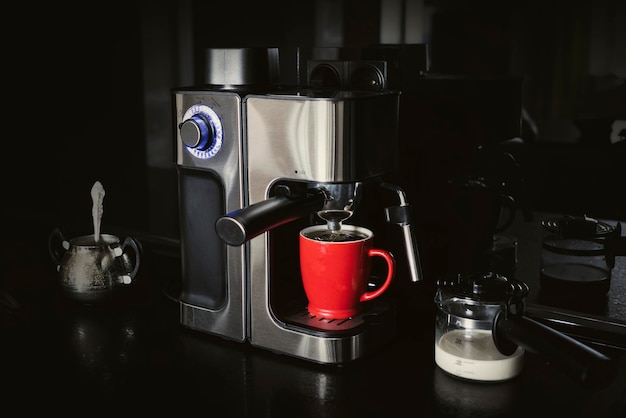 Macchina da caffè e tazza di latte su sfondo nero scuro per preparare il caffè a casa