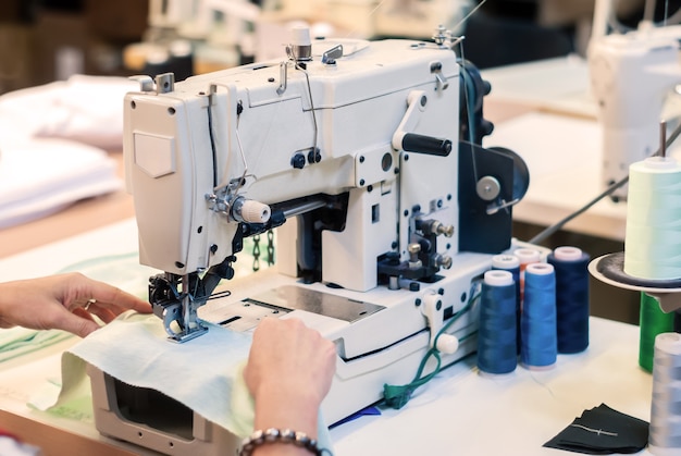 Macchina da cucire tagliacuci industriale e mani di sarta al lavoro nella fabbrica di abbigliamento