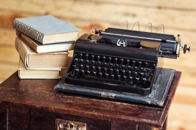 Macchina da scrivere d'epoca e libri sul tavolo con carta bianca sulla scrivania di legno