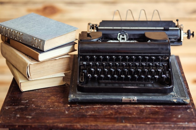 Macchina da scrivere d'epoca e libri sul tavolo con carta bianca sulla scrivania di legno