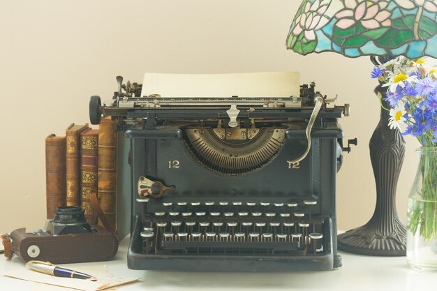 Macchina da scrivere vintage nera con libri sul tavolo di legno con lampada art nuveau si chiuda