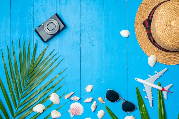 macchina fotografica, cappello, occhiali da sole e aereo su legno blu