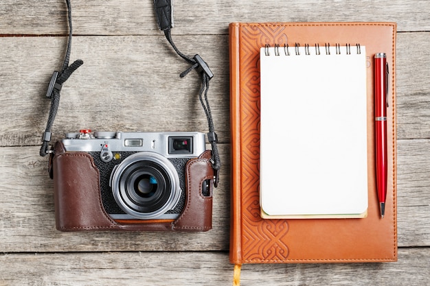 Macchina fotografica classica con la pagina in bianco del blocco note e penna rossa sullo scrittorio di legno e d'annata grigio con il telefono.