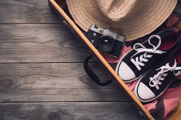 Macchina fotografica d'annata, cappello di paglia e scarpe da tennis in vecchia valigia sulla tavola di legno