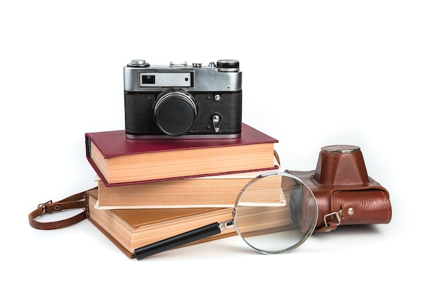 Macchina fotografica d'epoca, libri e lente di ingrandimento isolati su sfondo bianco. Vista laterale.