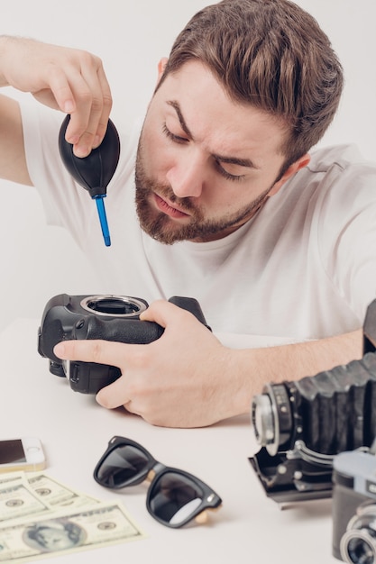 Macchina fotografica di pulizia del giovane fotografo con la pompa a vuoto. detergente per polvere a mano per fotocamera e obiettivi. luce soffusa