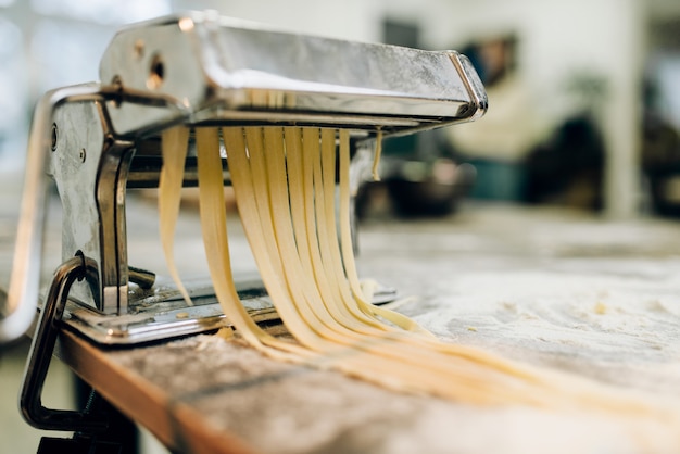 Macchina per pasta con pasta sul tavolo da cucina in legno cosparso di farina closeup. Cucina tradizionale italiana