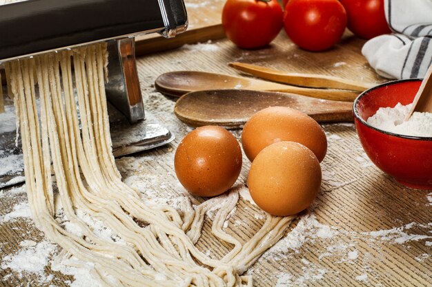 Macchina per pasta con tagliatelle e ingredienti su un tavolo di legno