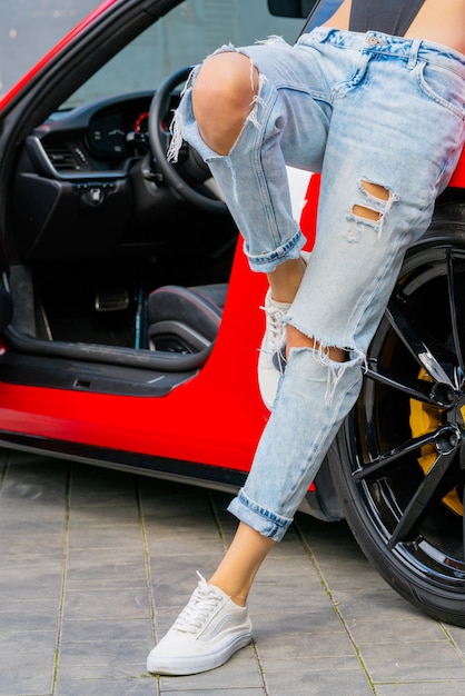 Macchina rossa e una ragazza in blue jeans. Stile giovanile moderno alla moda.