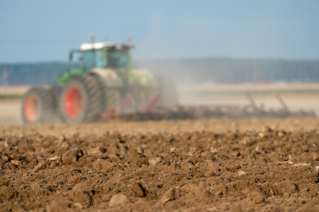 Macchine agricole lavora nel campo Un trattore con un aratro coltiva la terra prima di seminare grano e altri cereali Primo piano del terreno arato con messa a fuoco morbida Spazio vuoto per l'inserimento di testo