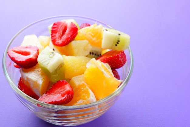 Macedonia di frutta vegetariana da ananas kiwi arancia e fragola su sfondo viola Frutta a fette in una ciotola trasparente Copia spazio