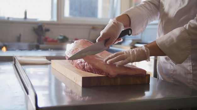 Macellaio che taglia un grande pezzo di carne fresca cruda che giace su una tavola di legno in una cucina commerciale, cucina e concetto di alta cucina