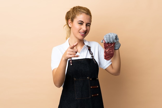 Macellaio donna che indossa un grembiule e che serve carne fresca tagliata sopra il muro punta il dito contro di te