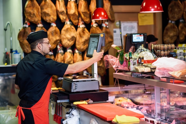 Macellaio in una macelleria che appesantisce la carne e carica