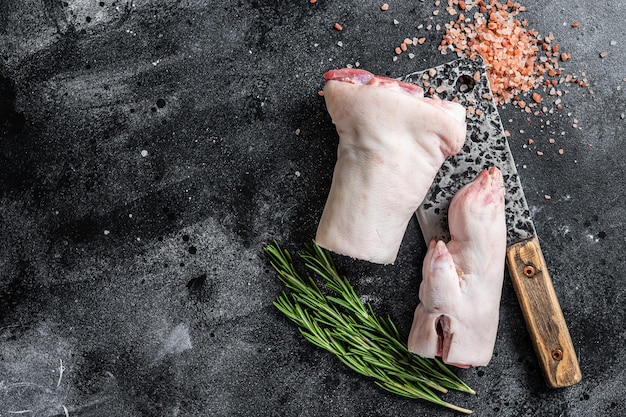 Macelleria di carne di maiale crudo piedi di zoccolo su una tavola da taglio sfondo nero vista superiore spazio di copia.