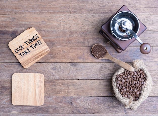 Macinacaffè, beens del caffè in tela da imballaggio e piatto di legno in bianco sulla tavola di legno, disposizione piana con lo spazio della copia